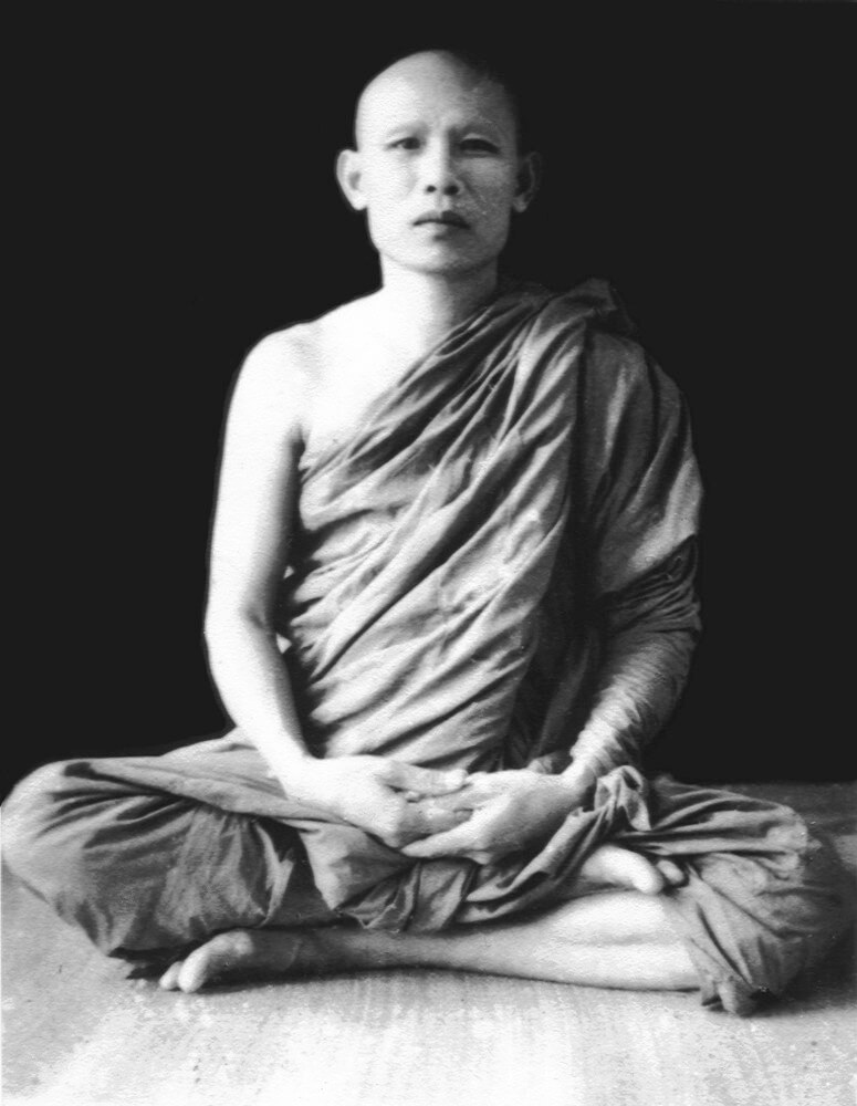 Photo of Ajaan Lee Dhammadharo sitting cross-legged on wooden platform